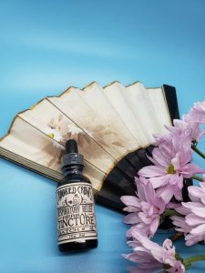 Crooked Crows tincture bottle with a paper fan and pink flowers