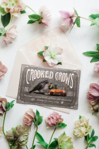 Crooked Crows card among pink flowers on white